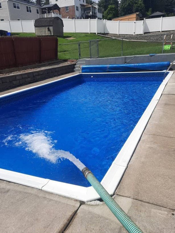 Pool after: new white coping and liner, filling with blue water from the same viewpoint