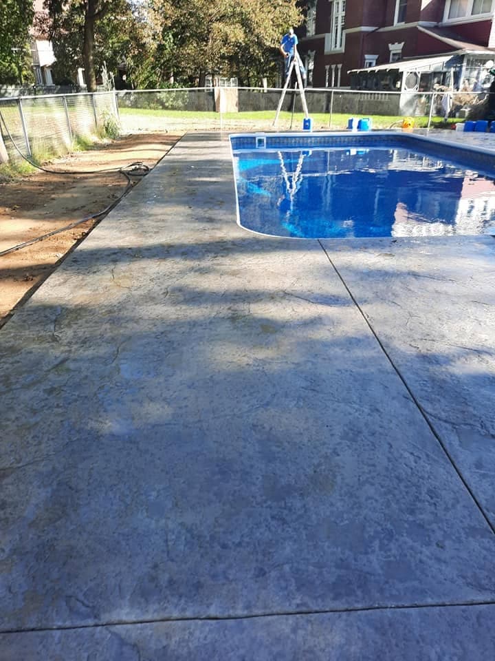 Pool after: filled blue pool surrounded by new stamped concrete decking from the same viewpoint