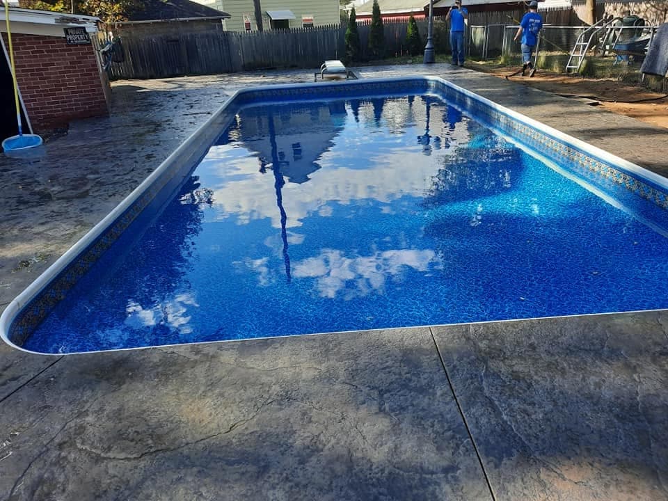 Finished pool with deep blue liner surrounded by stamped concrete, Pool Dogz crew in the background