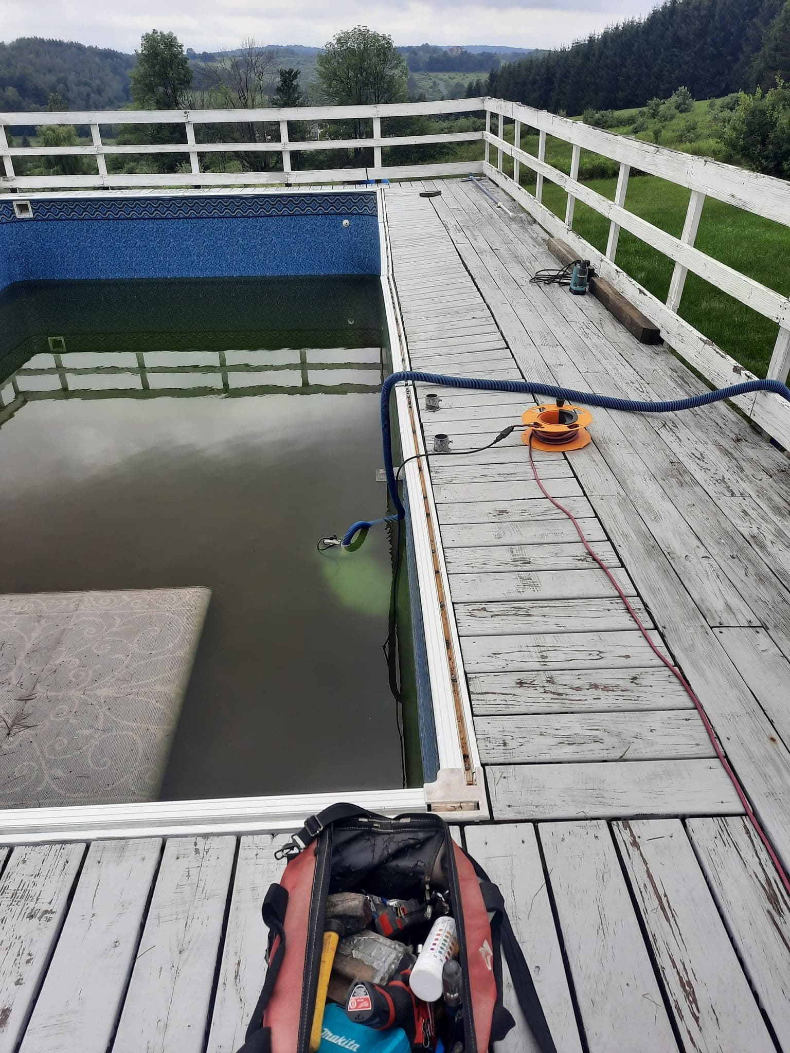 Pool before: murky green water and an aging liner in a deck-surrounded pool